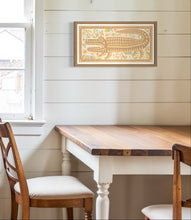 Load image into Gallery viewer, David Wien archival  print of the Beast fine art painting, an alligator figure with light brown and neutral tones surrounded by folk art style flowers in a medium brown frame shown in a country kitchen that has cream white walls and shiplap
