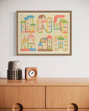 Load image into Gallery viewer, David Wien folk art print of pastel and neutral buildings in a medium tone interior with a modern clock and dresser
